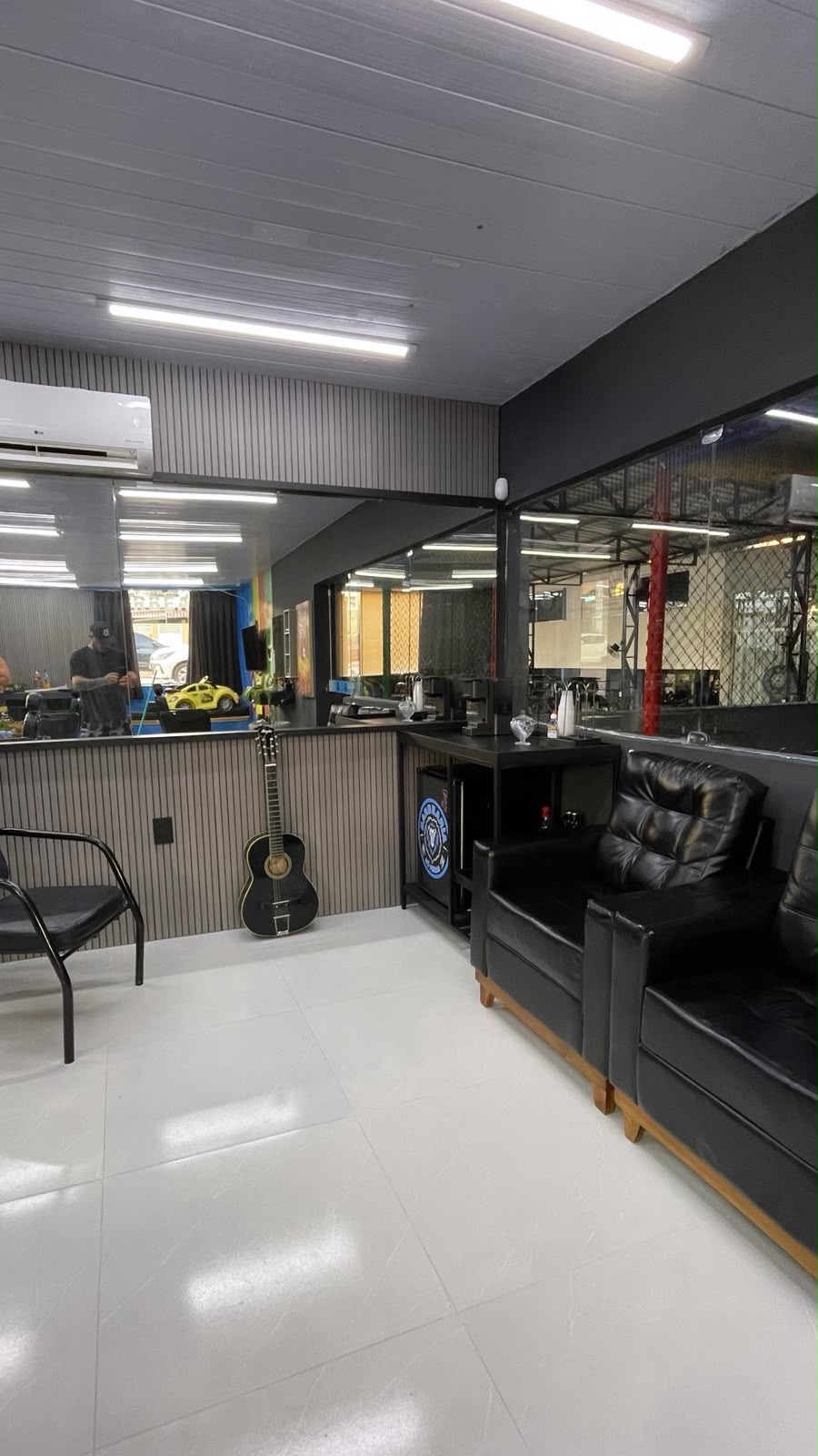 Área de espera da Barbearia Só Feras, com sofá preto, espelhos e guitarra
